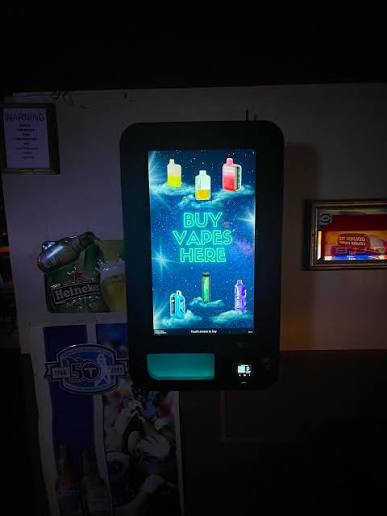 Wall-mounted vending screen advertising vapes inside a bar